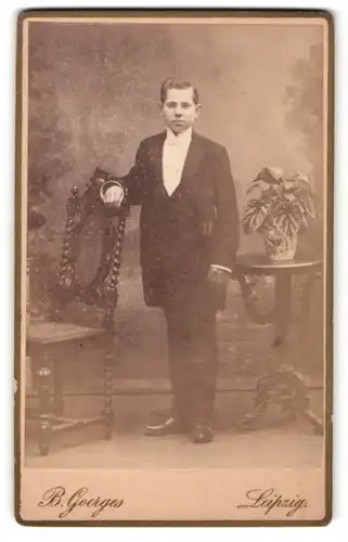 Fotografie B. Goerges, Leipzig, Portrait junger Herr mit Fliege im Anzug an Stuhl gelehnt