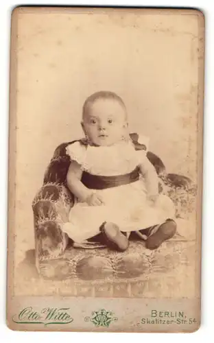 Fotografie Otto Witte, Berlin, Portrait niedliches Kleinkind im weissen Kleid auf Sessel sitzend