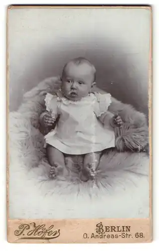 Fotografie P. Höfer, Berlin, Portrait niedliches Baby im weissen Kleid auf Fell sitzend