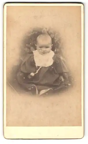 Fotografie unbekannter Fotograf und Ort, Portrait niedliches Baby mit Latz im hübschen Kleid auf Kissen sitzend