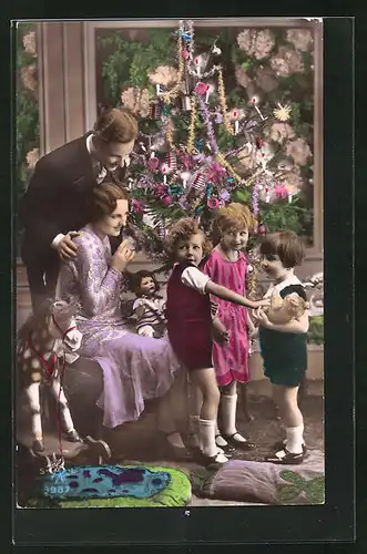 Foto-AK Familie mit Kindern u. Teddy, Puppe und Spielzeugpferd am Tannenbaum