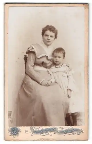 Fotografie A. Jandorf & Co., Berlin, Portrait junge Dame im modischen Kleid auf Stuhl sitzend mit Mädchen an der Hand