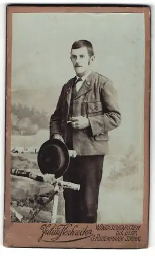 Fotografie Julius Hochreiter, Windischgarten Ob. Östr. & Rottenmann Strmk., Portrait junger Herr mit Hut an Zaun gelehnt