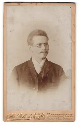 Fotografie Otto Liebert, Holzminden, Höxter & Bad-Driburg, Portrait charmanter Herr mit Brille u. Zwirbelbart im Anzug