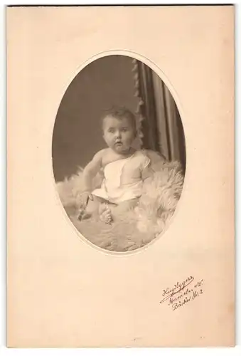 Fotografie Hugo Eggers, Hameln a / W., Portrait niedliches Baby im weissen Hemd auf Fell sitzend