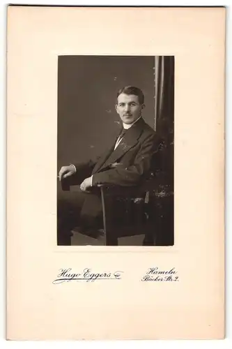 Fotografie Hugo Eggers, Hameln, Portrait charmanter Herr im Anzug auf Stuhl sitzend