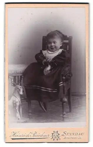 Fotografie Heinrich Reichner, Berlin-Spandau, Portrait lachendes kleines Mädchen mit Spielzeugpferd