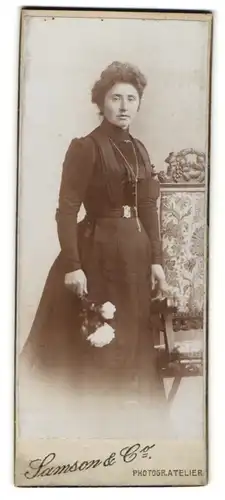 Fotografie Samson & Co., unbekannter Ort, Portrait bürgerliche Dame im eleganten Kleid mit Blumen an Stuhl gelehnt