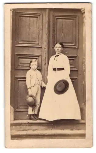 Fotografie G. Hisgen, Lich, Dame mit Gürtel um Taille und Hut haltend mit Jungen Hut haltend vor Tür