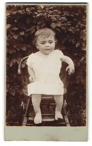 Fotografie unbekannter Fotograf und Ort, Portrait niedliches Kleinkind im weissen Kleid im Hochstuhl sitzend