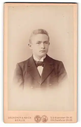 Fotografie Grundner & Abich, Berlin, Portrait junger Mann im Anzug mit Fliege