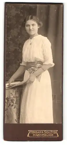 Fotografie Hermann Schlüter, Magdeburg, Portrait junge Dame im weissen Kleid mit Bildern an Tisch gelehnt