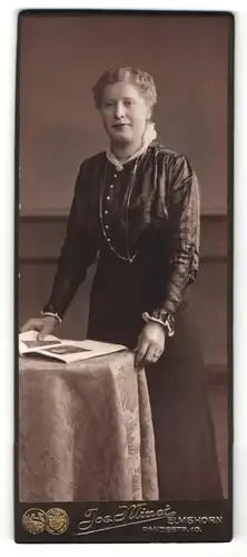 Fotografie Jos. Minet, Elmshorn, Portrait bürgerliche Dame in eleganter Bluse mit Zeitung an Tisch gelehnt