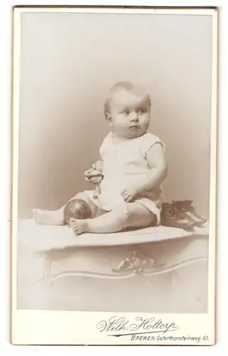 Fotografie Wilh. Holtorp, Bremen, Portrait blondes niedliches Kleinkind mit Bällen im weissen Kleidchen