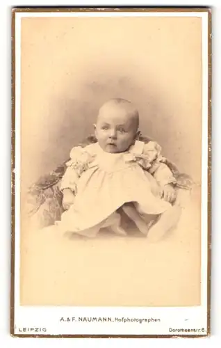 Fotografie A. & F. Naumann, Leipzig, Portrait zuckersüsses Baby im weissen Taufkleidchen mit Schleifen