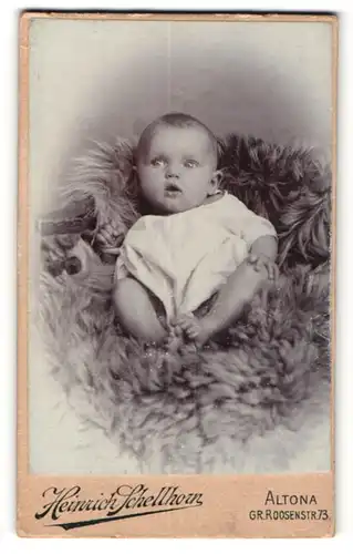 Fotografie Heinrich Schellhorn, Altona, Portrait niedliches Baby im weissen Hemd auf Fell sitzend