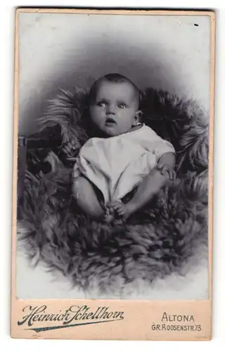 Fotografie Heinrich Schellhorn, Altona, Portrait niedliches Baby im weissen Hemd auf Fell sitzend