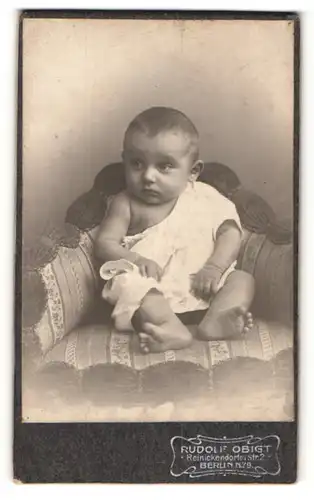 Fotografie Rudolf Obigt, Berlin, Portrait niedliches Kleinkind im weissen Hemd auf Sessel sitzend