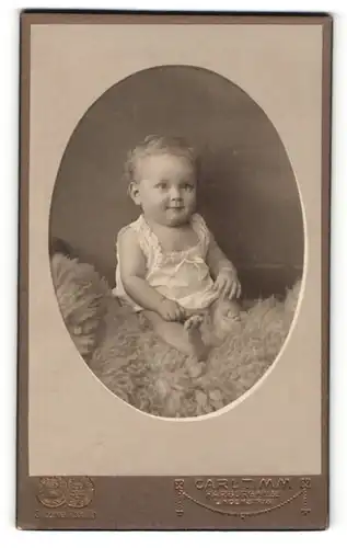 Fotografie Carl Timm, Harburg a / Elbe, Portrait niedliches Kleinkind im weissen Hemd auf Fell sitzend
