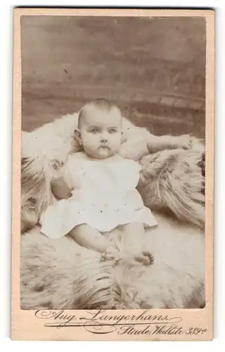 Fotografie Aug. Langerhans, Stade, Portrait niedliches Baby im weissen Hemd auf Fell sitzend