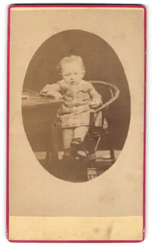 Fotografie unbekannter Fotograf und Ort, Portrait niedliches Kleinkind in hübscher Kleidung am Tisch sitzend