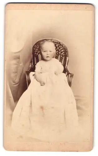 Fotografie Hans Styx, Giessen, Kleinkind im weissen Kleid auf einem Korbstuhl