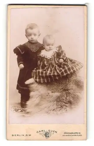 Fotografie Carl Euen, Berlin-SW, Portrait niedliches Kleinkind im karierten Kleid auf Fell sitzend u. Geschwisterkind