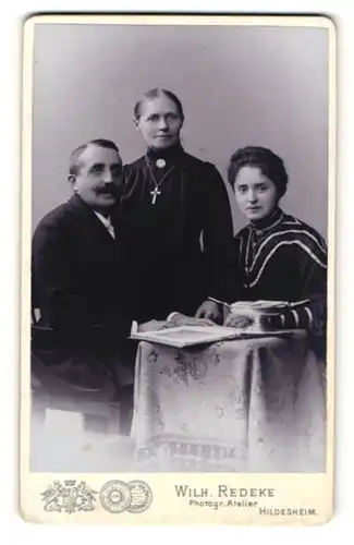 Fotografie Wilh. Redeke, Hildesheim, Portrait bürgerliche Familie mit älterer Tochter mit Buch am Tisch sitzend