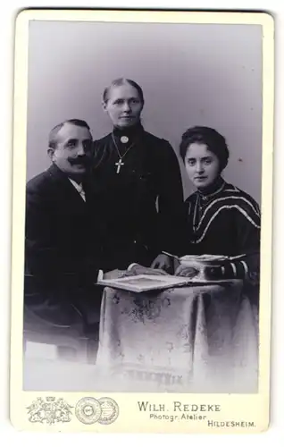 Fotografie Wilh. Redeke, Hildesheim, Portrait bürgerliche Familie mit älterer Tochter mit Buch am Tisch sitzend
