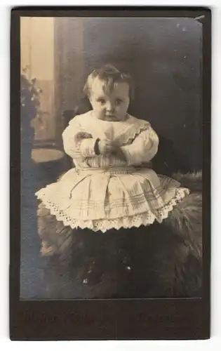 Fotografie Walter Müller, Paderborn, Baby im Kleidchen auf Fell sitzend