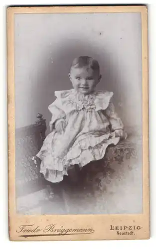 Fotografie Friedr. Brüggemann, Leipzig, Baby in Kleid mit leichtem Lächeln