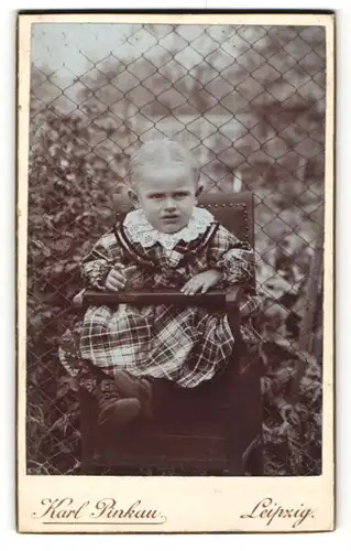 Fotografie Karl Pinkau, Leipzig, kleines Mädchen in kariertem Kleid in Kinderstuhl vor Zaun