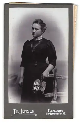 Fotografie Th. Jensen, Flensburg, Portrait junge Dame im eleganten Kleid mit Blumen an Zaun gelehnt