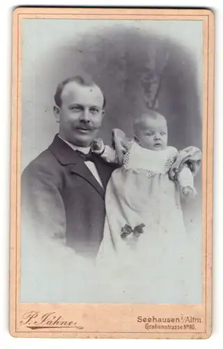 Fotografie P. Jähne, Seehausen i. Altm., Vater im Anzug hält sein Kind in gepufftem Kleidchen im Arm
