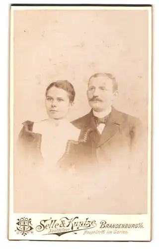 Fotografie Selle & Kuntze, Brandenburg a. H., Junge Frau in gepufftem Kleid und Mann mit Schnurrbart im Anzug