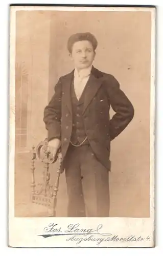 Fotografie Jos. Lang, Augsburg, Portrait dunkelhaariger junger Mann im ANzug am Stuhl stehend