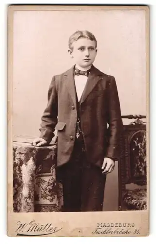 Fotografie W. Müller, Magdeburg, Portrait hübscher Knabe im Anzug an Tisch gelehnt