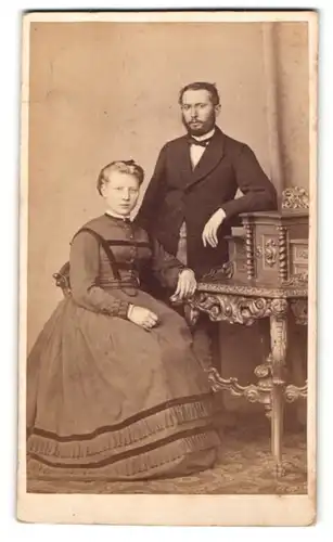 Fotografie Julius Giere, Hannover, Portrait junge Dame im eleganten Kleid am Tisch sitzend u. Herr im Anzug