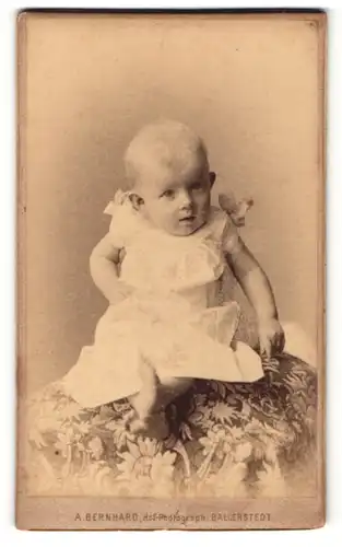 Fotografie A. Bernhard, Ballenstedt, Baby im weissen Kleid sitzend auf einem Kissen