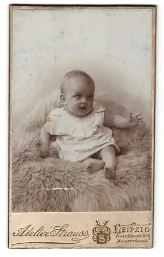 Fotografie Atelier Strauss, Leipzig, Portrait niedliches Baby im weissen Hemd auf Fell sitzend