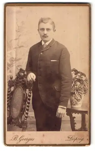 Fotografie B. Goerges, Leipzig, Portrait bürgerlicher Herr mit Zwirbelbart im Anzug an Stuhl gelehnt