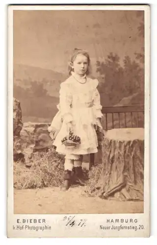 Fotografie E. Bieber, Hamburg, Portrait kleines Mädchen im hübschen Kleid mit Körbchen an Bank gelehnt