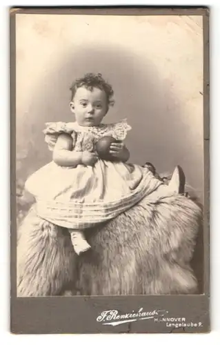 Fotografie F. Renziehausen, Hannover, Portrait niedliches Kleinkind im hübschen Kleid mit Ball auf Fell sitzend