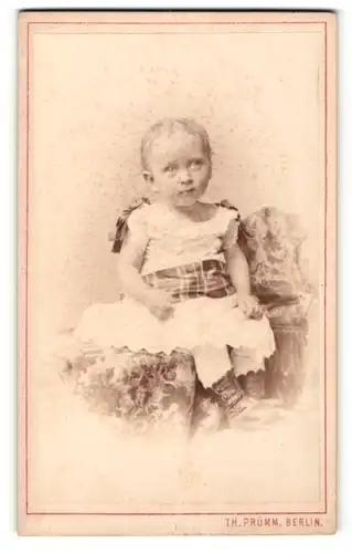Fotografie Th. Prümm, Berlin, Portrait kleines Mädchen im hübschen Kleid auf Decke sitzend