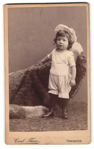 Fotografie Carl Thies, Hannover, Portrait niedliches Kleinkind im weissen Hemd an Sessel gelehnt
