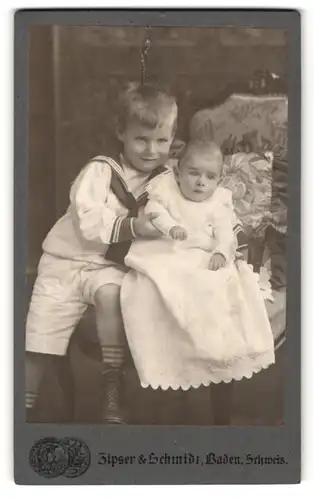 Fotografie Zipser & Schmidt, Baden, Portrait Baby im weissen Kleid u. Bruder im Matrosenanzug auf Sessel sitzend