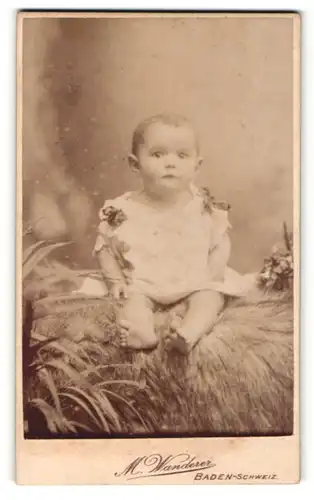 Fotografie M. Wanderer, Baden-Schweiz, Portrait niedliches Kleinkind im weissen Hemd auf Fell sitzend