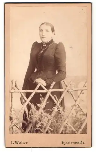 Fotografie L. Wolter, Finsterwalde, Portrait junge Dame im eleganten Kleid mit Kreuzkette an Zaun gelehnt