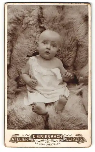 Fotografie C. Griesbach, Leipzig, Portrait niedliches Baby im weissen Hemdchen auf Fell sitzend