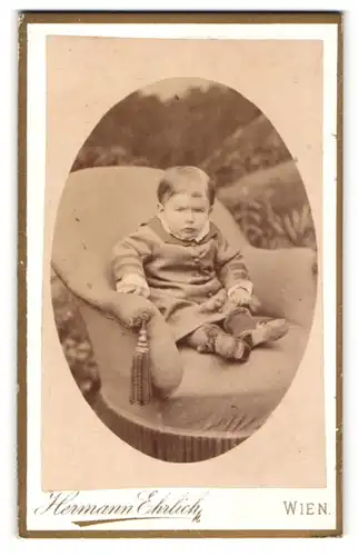 Fotografie Hermann Ehrlich, Wien, Portrait Kleinkind in Mantel auf Sitzmöbel